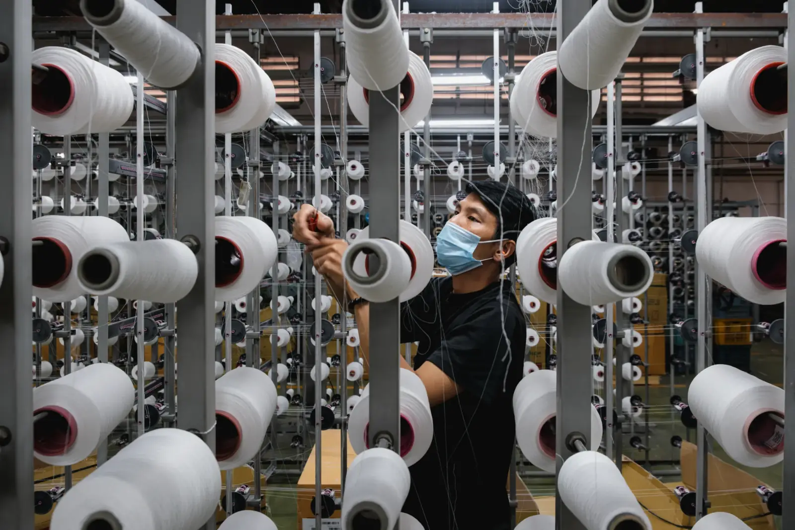 Worker adjusting yarn machinery on a factory floor